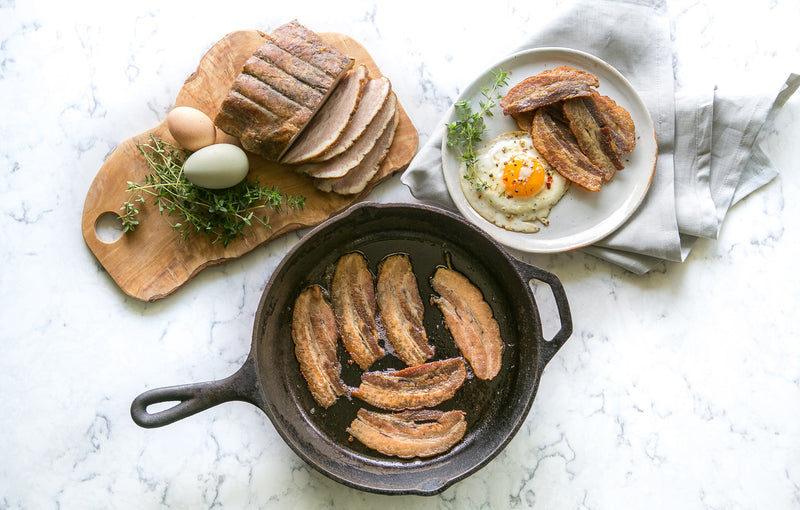 Pete's Bacon - bacon on a cutting board with eggs before preparation, bacon frying in a cast iron pan, prepared bacon and egg plate